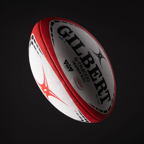 A Gilbert rugby ball, red and white, floats against a black background.