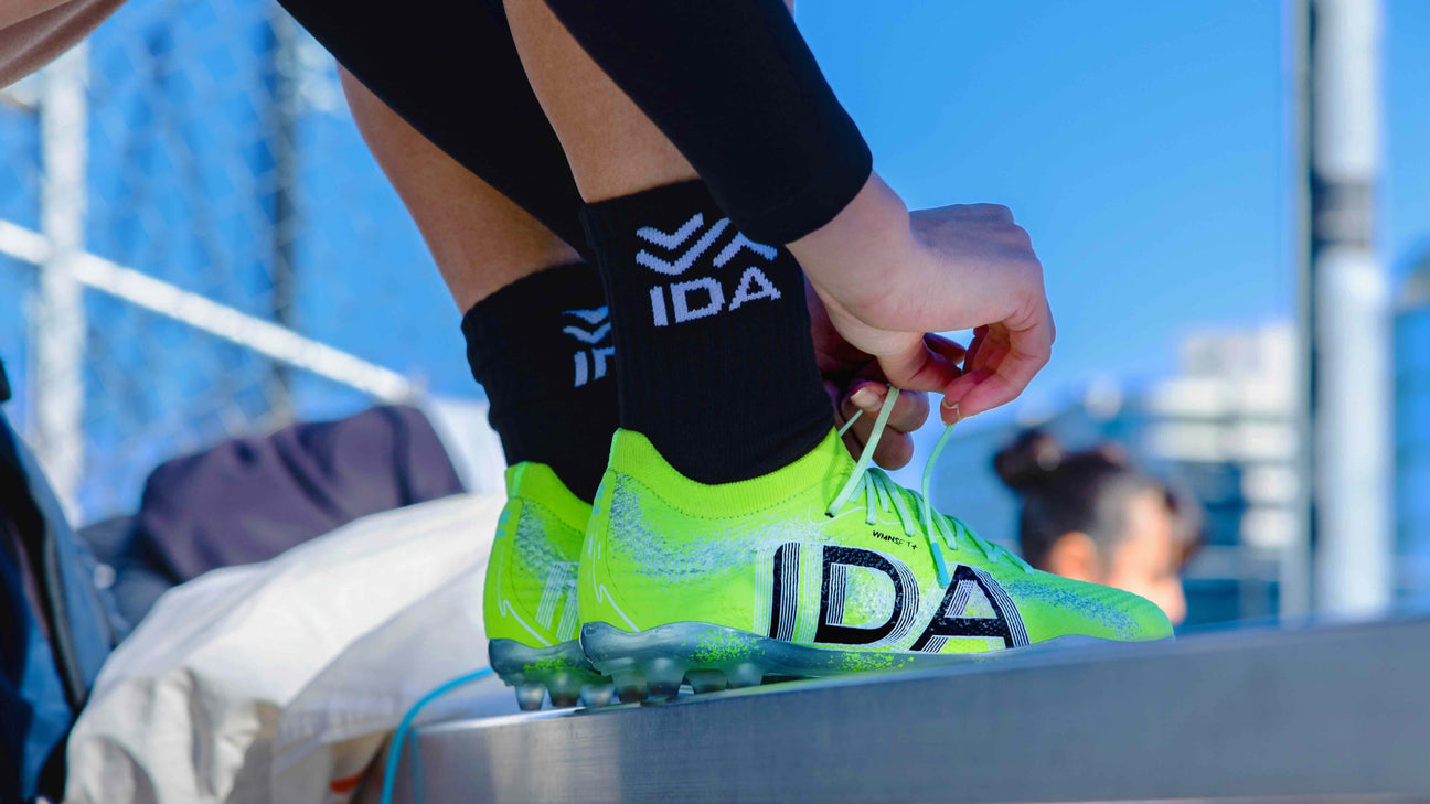 Person tying laces on bright green soccer cleats with "IDA" logo.