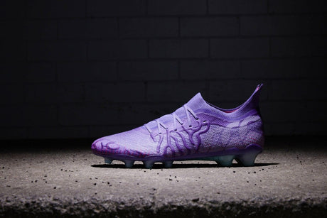 A single purple soccer cleat illuminated against a dark background with a brick wall.