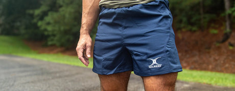 Close-up of a man wearing dark sports shorts and a burgundy t-shirt, standing against a neutral background with the word "shorts" superimposed.