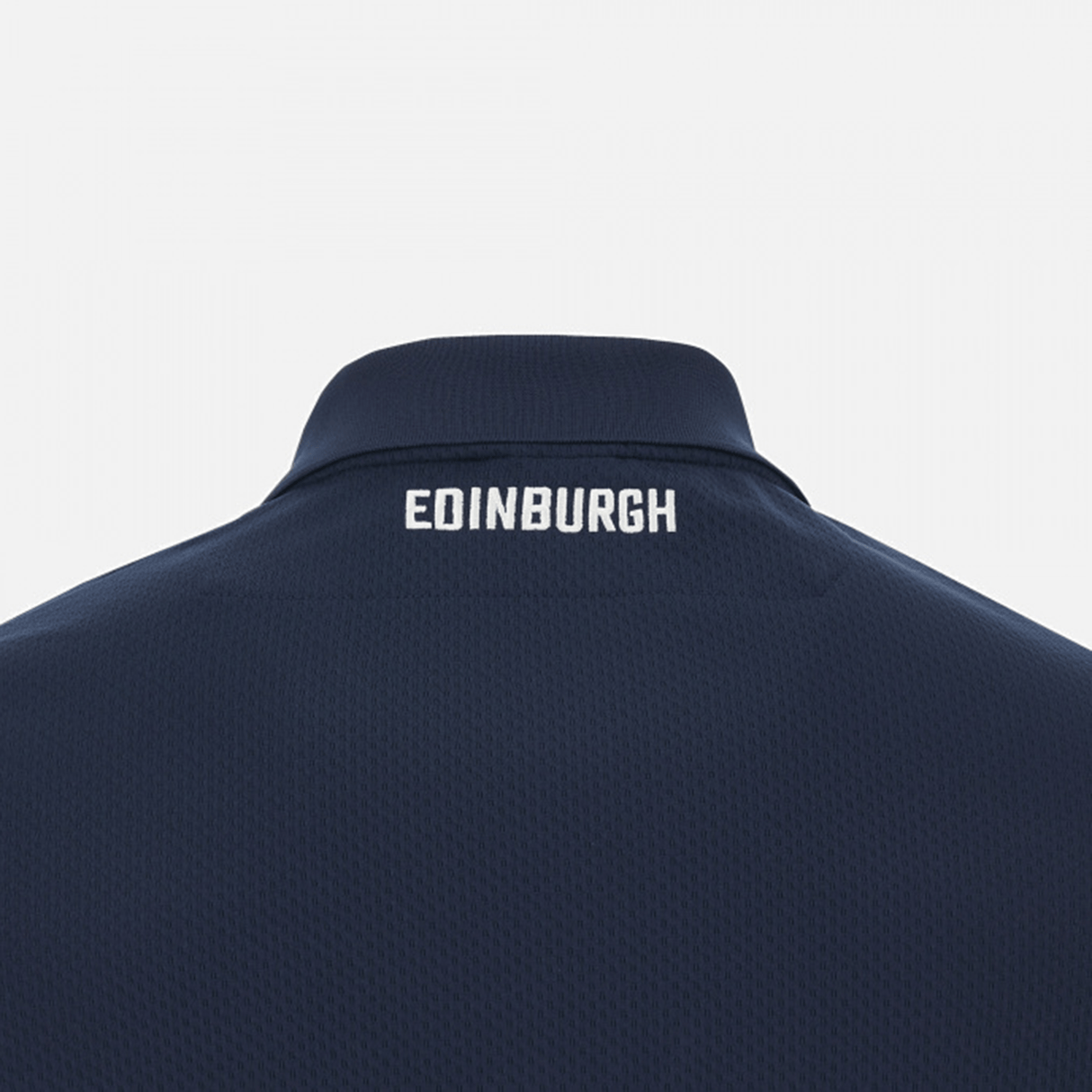 Back of a dark blue jacket with "Edinburgh Rugby 23/24 Player Travel Polo by Macron" embroidered across the neckline in white text.