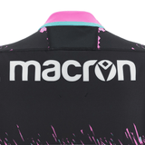 Close-up of the back of a Barbarians 23/24 Training Jersey by Macron featuring moisture-wicking technology, with the Macron logo prominently displayed. It has a black base and pink details on the collar and edges.