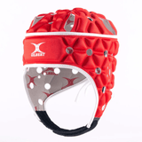 The Gilbert Air Headguard by Gilbert is a red helmet with white lining, a black chin strap, hexagonal padded design for shock absorption, and ventilation holes.