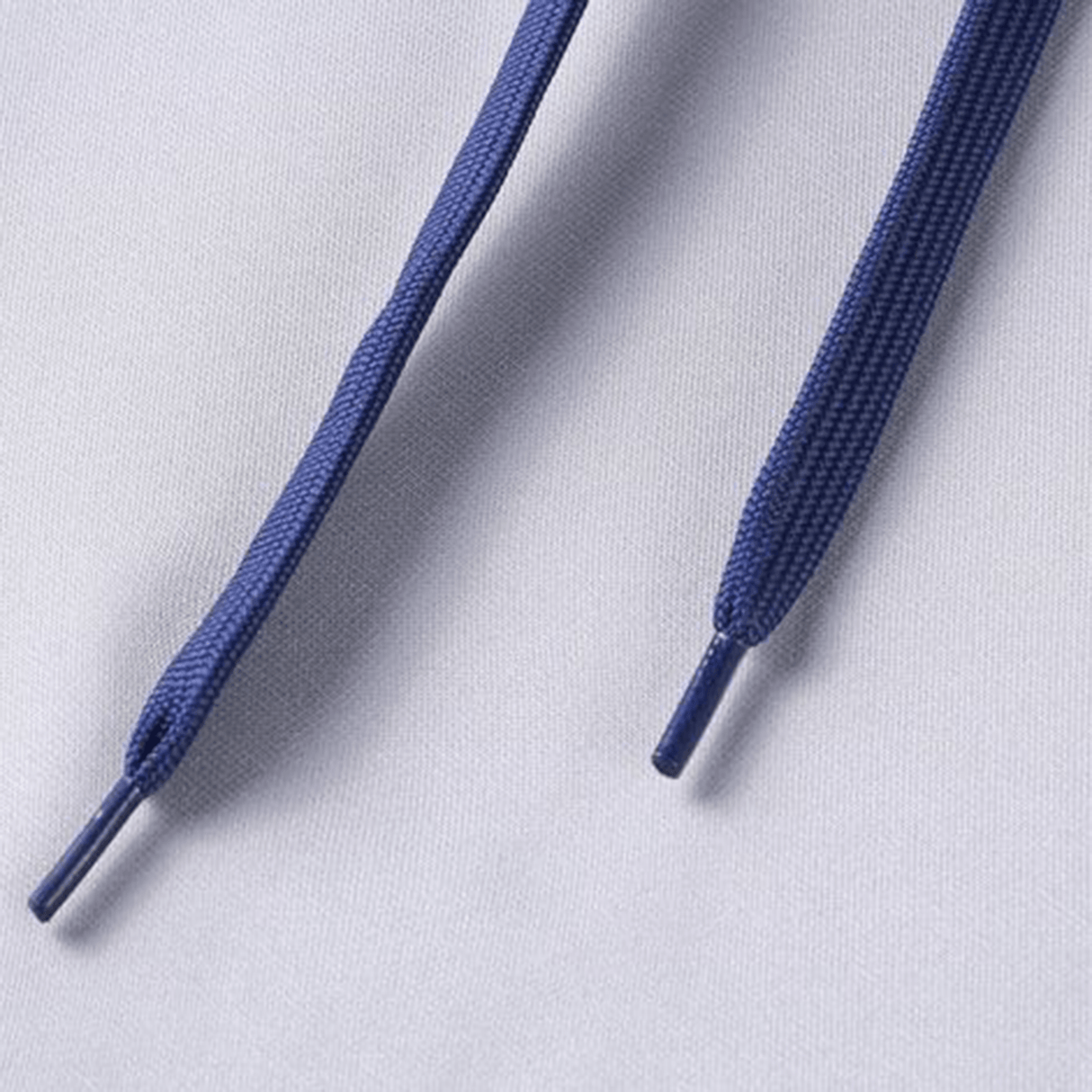 Close-up image of two blue shoelaces with plastic aglets on a pale gray background, reminiscent of the vibrant hue found on a Classic Sportswear Blues Super Rugby Supporters Hoodie 24.