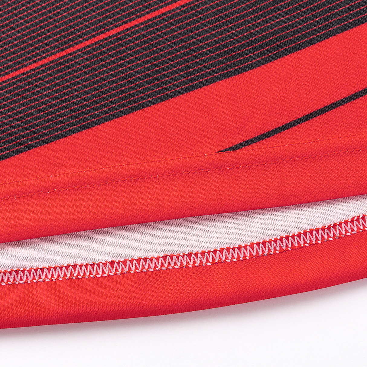 Close-up of red fabric with black linear design, similar to the Crusaders Super Rugby Replica Home Jersey 25/26 by Classic Sportswear, showing a folded hem with white stitching.