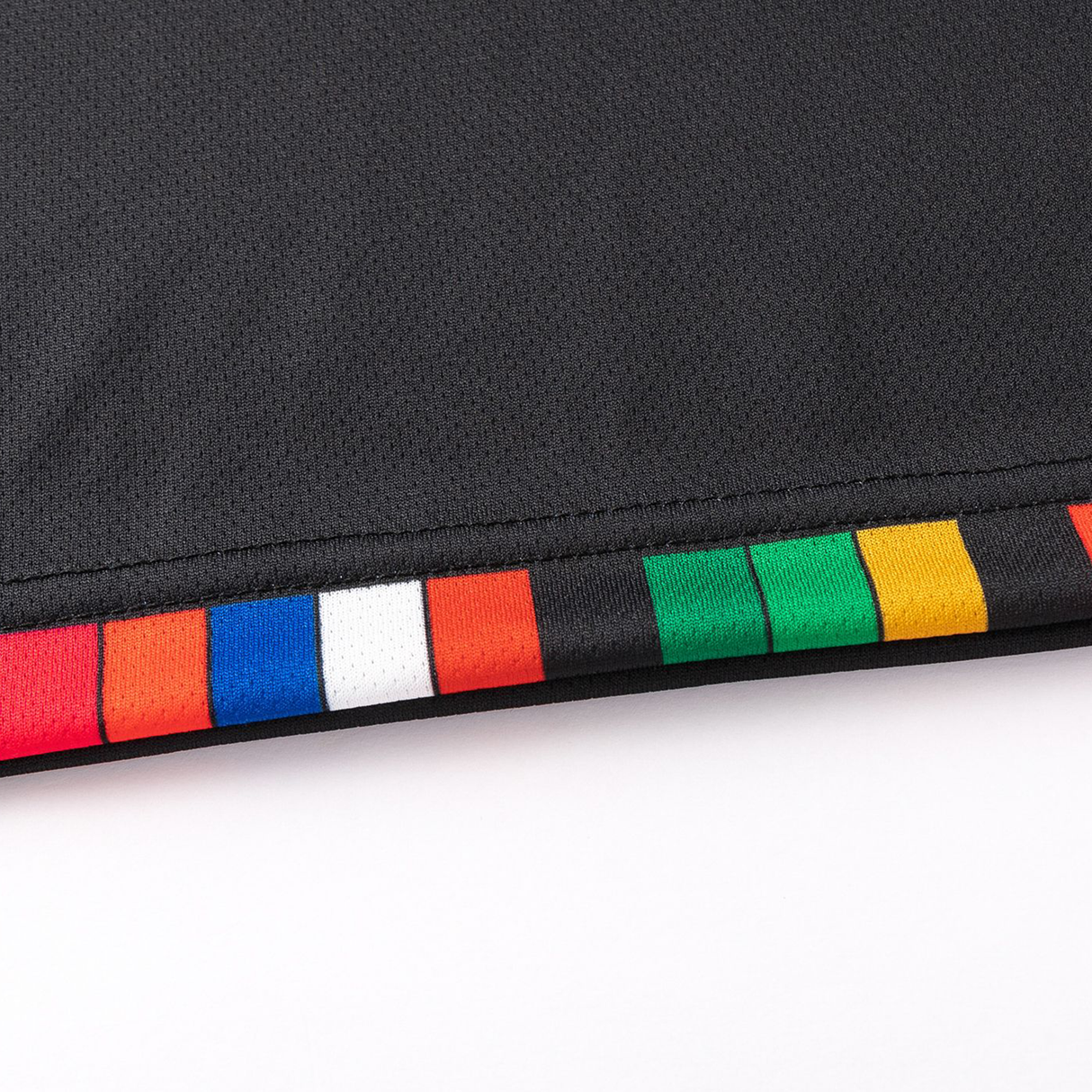 Close-up of a black, moisture-wicking fabric with a hem showcasing colored blocks: orange, blue, white, red, black, green, and yellow. The dynamic design reflects the sporty elegance of the Crusaders Super Rugby Team Polo 25/26 by Classic Sportswear.