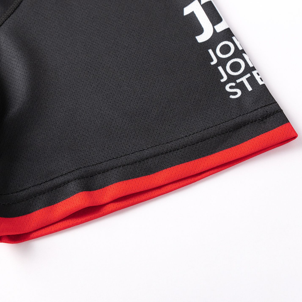 Close-up of a Crusaders Super Rugby Team Polo 25/26 by Classic Sportswear sleeve, featuring red-trimmed black fabric and partially visible white embroidered logos, made from moisture-wicking material.