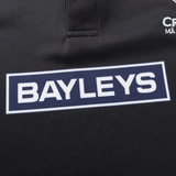 Close-up of a black sports jersey from Classic Sportswear's "Crusaders Super Rugby Team Polo 25/26," featuring the "BAYLEYS" logo in white within a navy rectangle, crafted with moisture-wicking fabric.