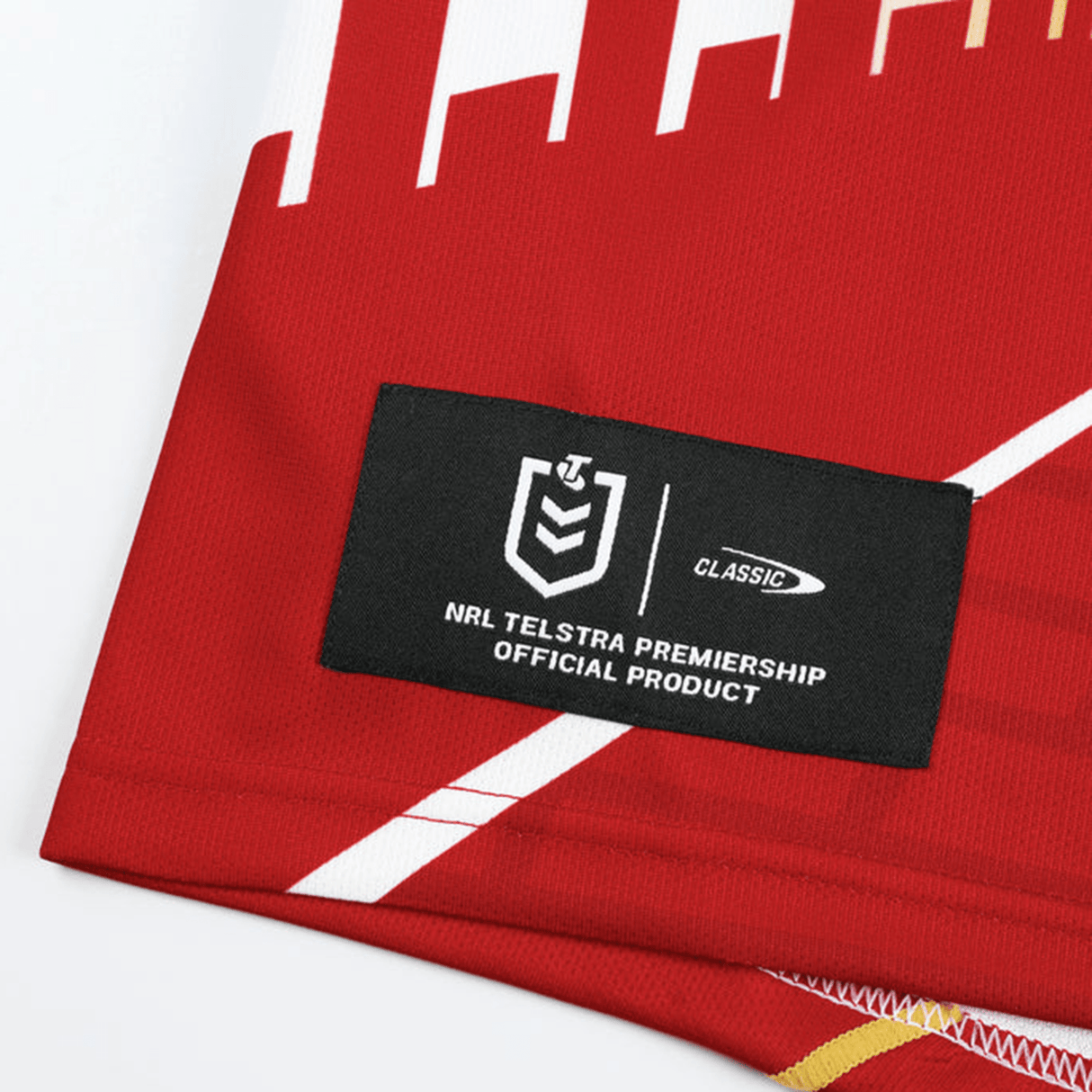 Close-up of an official NRL Telstra Premiership product label sewn onto a red Classic Sportswear garment with white and yellow accents, likely part of the Dolphins NRL Heritage Jersey by Classic Sportswear collection available on ANZAC Avenue.