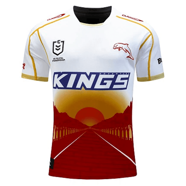 A white Dolphins NRL Heritage Jersey by Classic Sportswear with yellow and maroon accents features the logo "KINGS" across the front, a dolphin graphic, and a sunset backdrop with silhouettes of arches leading into ANZAC Avenue.