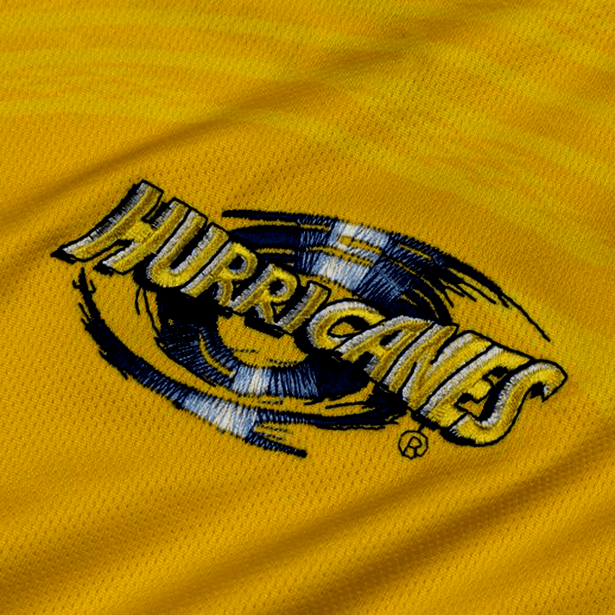 Embroidered logo of the "Hurricanes Super Rugby 2024 Home Jersey" by Classic Sportswear with a stylized eye design on a yellow fabric background.