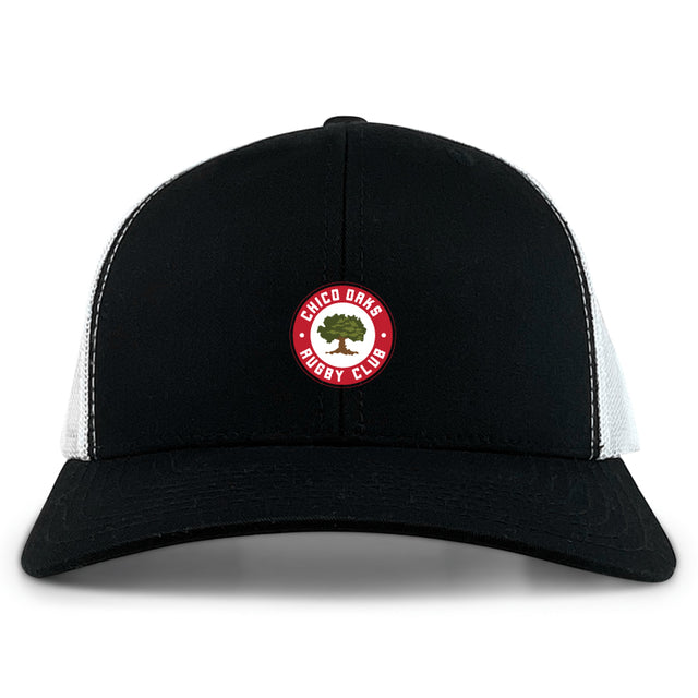 The Chico Oaks Retro Trucker Cap by EMB Alpha Broder is a black and white cap with an embroidered "Chico Oaks Rugby Club" logo on the front, featuring a handy snapback closure for an adjustable fit.