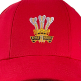 The Wales Rugby 1976 Triple Crown Cap by Ellis Rugby is a red cap adorned with an embroidered emblem celebrating the team's 1976 achievement. It features three white feathers and the words "Ich Dien" in gold, honoring Welsh rugby history.