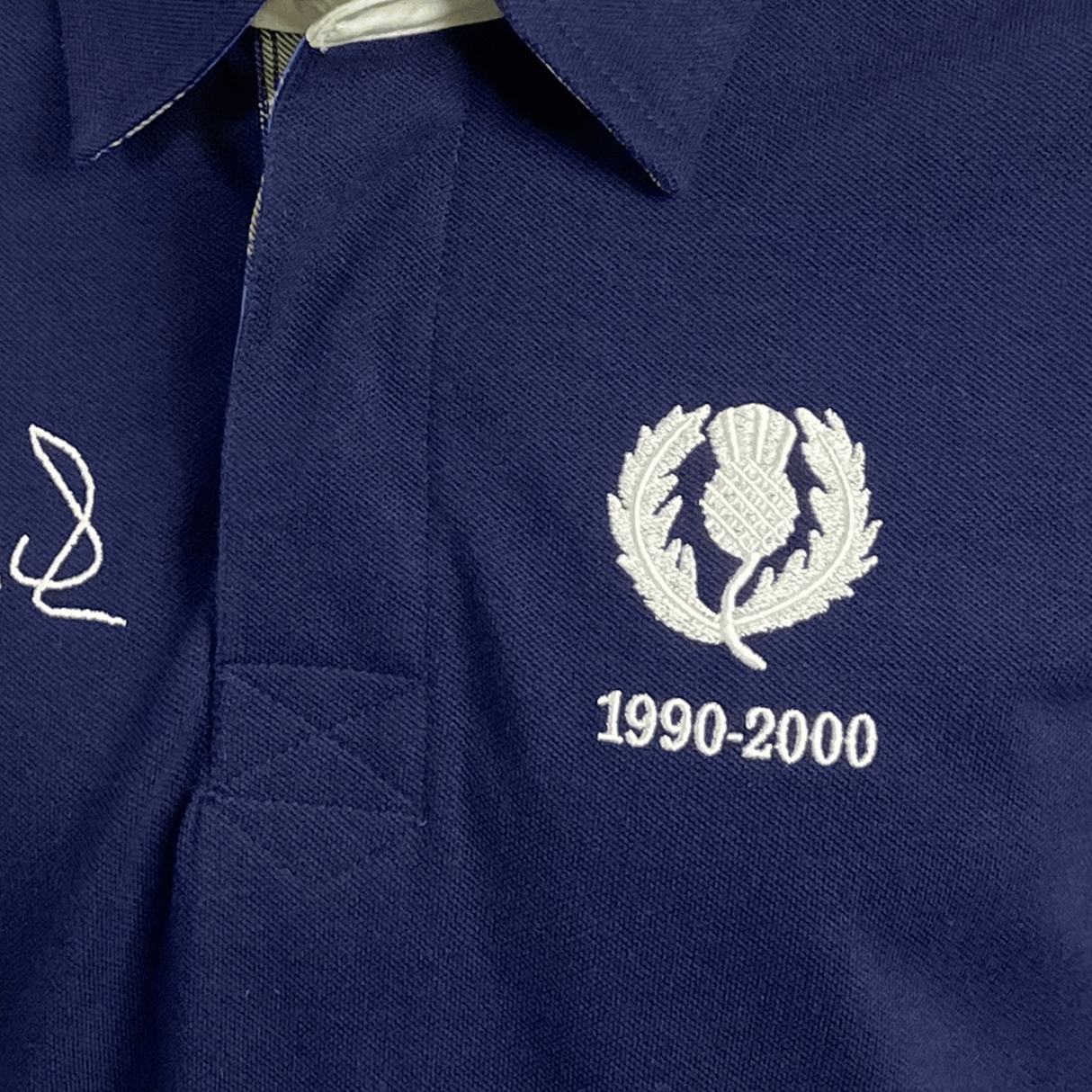 A blue Doddie Weir Polo by Ellis Rugby with the scottish thistle embroidered on it.