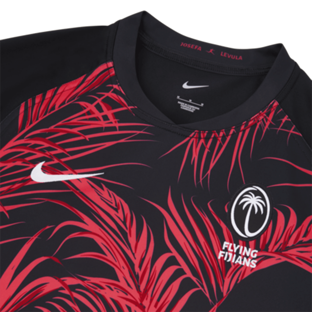 Close-up of the Fiji 24/25 Replica Away Jersey by Nike showcasing red palm leaf patterns, a white palm logo with "Flying Fijians," and the iconic Nike swoosh on a black background.