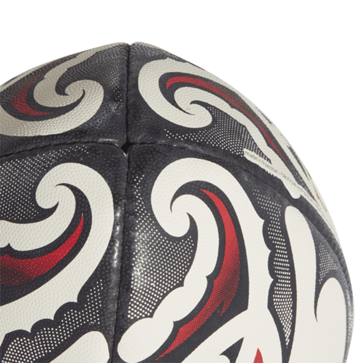 Close-up of the All Blacks Replica Ball by adidas, showcasing a black, white, and red intricate Maori pattern design. The stitches and texture of this adidas replica are clearly visible.