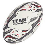 A white "All Blacks Replica Ball by adidas" adorned with black and red Maori patterns and a striking fern logo, crafted by adidas.