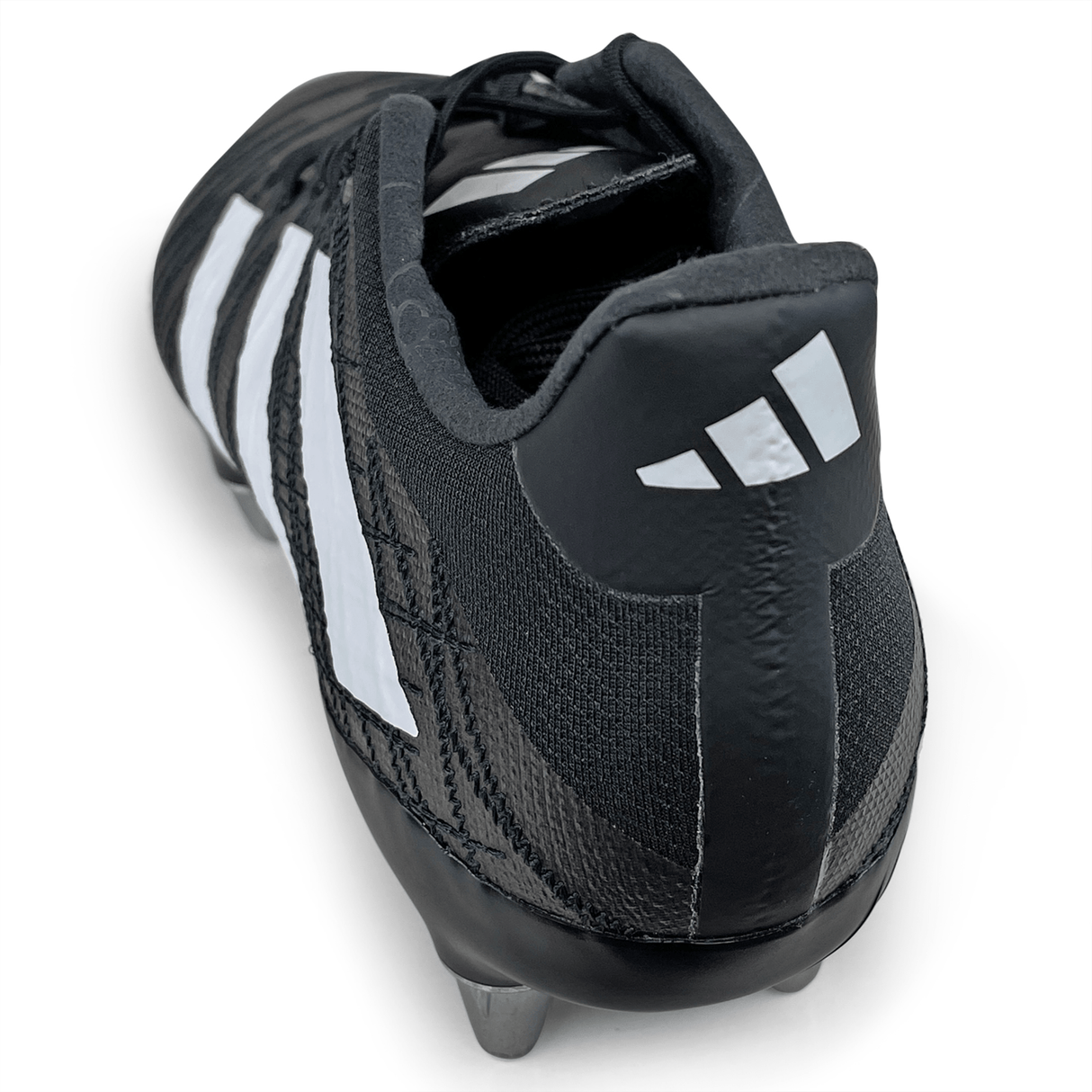 A close-up view of the adidas Kakari Z.1 SG 23 rugby cleat showcases its core black exterior with white stripes and metal studs on the sole, viewed from the heel.