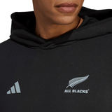 Close-up of a person wearing the All Blacks Supporters Pull Over Hoodie by adidas, featuring the iconic "All Blacks" logo, a fern leaf design, and the adidas 3 Bar Logo on the front—perfect for rugby supporters.