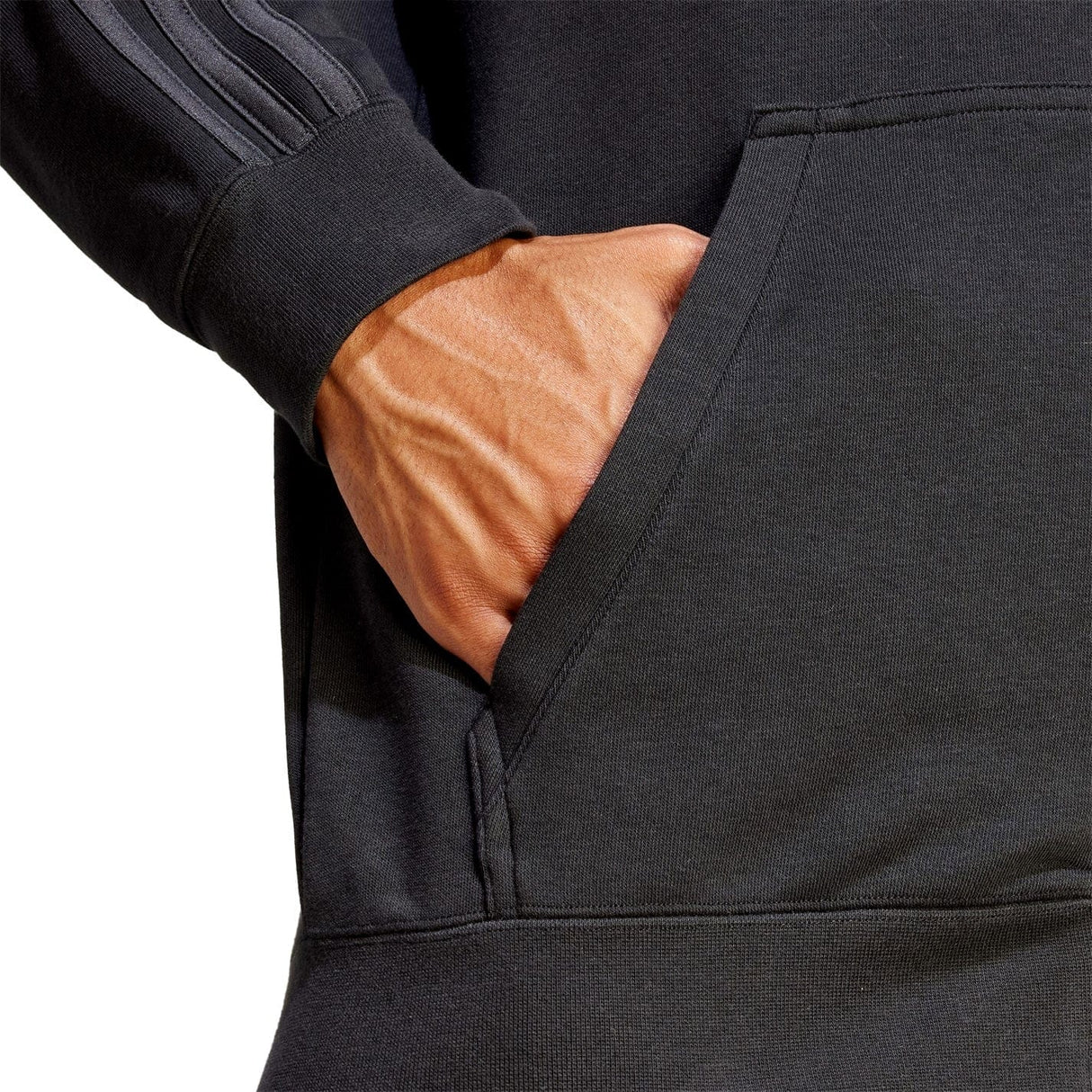 Close-up of a person's hand placed in the pocket of a dark-colored All Blacks Supporter Full-Zip Hoodie by adidas, showcasing striped detail on the sleeve and made from soft French terry fabric.