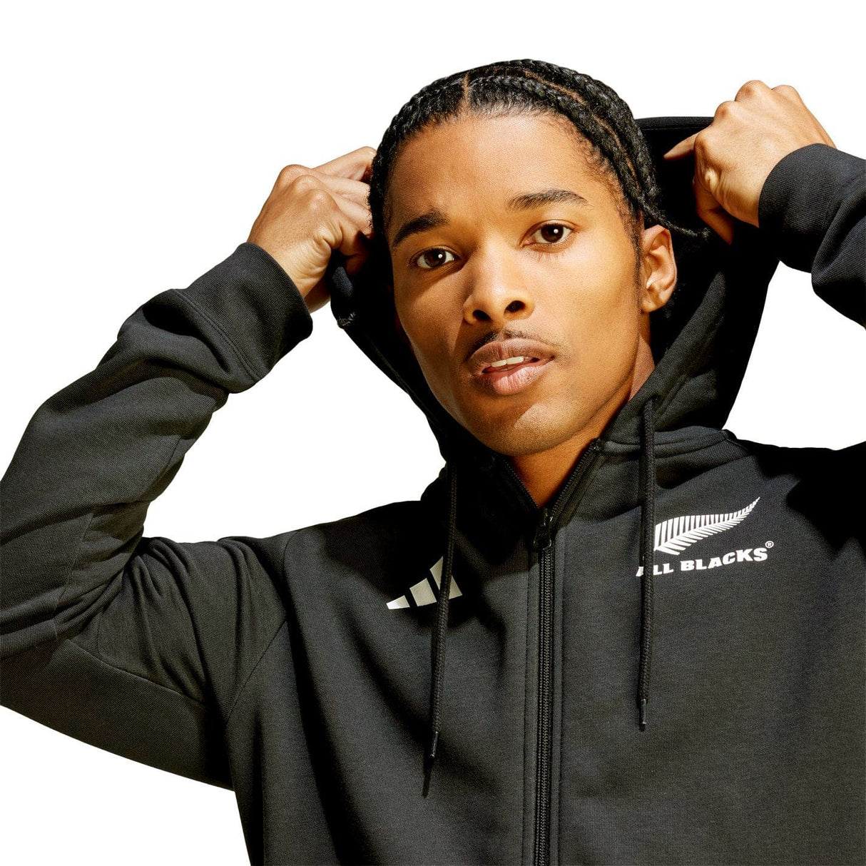 A person wearing an adidas All Blacks Supporter Full-Zip Hoodie in black, made from soft French terry fabric, with the adjustable hood partially pulled up, looking directly at the camera.