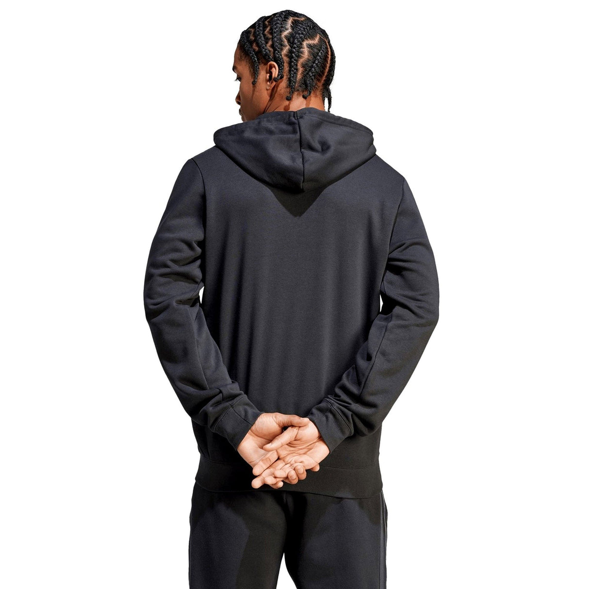 Person with braided hair wearing an adidas All Blacks Supporter Full-Zip Hoodie made from French terry fabric and black pants, seen from the back with hands clasped behind.