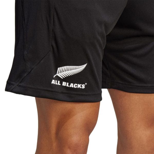 Close-up of a person's legs wearing the All Blacks Gym Short by adidas, featuring the New Zealand All Blacks logo and a white fern emblem on the side, designed with moisture-wicking AEROREADY technology.