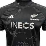 The All Blacks Performance Tee by adidas features "ALL BLACKS" and a silver fern logo on the right side, "INEOS" prominently displayed in the center, and another logo with three white stripes on the left side. This black sports jersey is made with moisture-wicking AEROREADY to keep you comfortable and includes a subtle floral design as well as recycled materials.