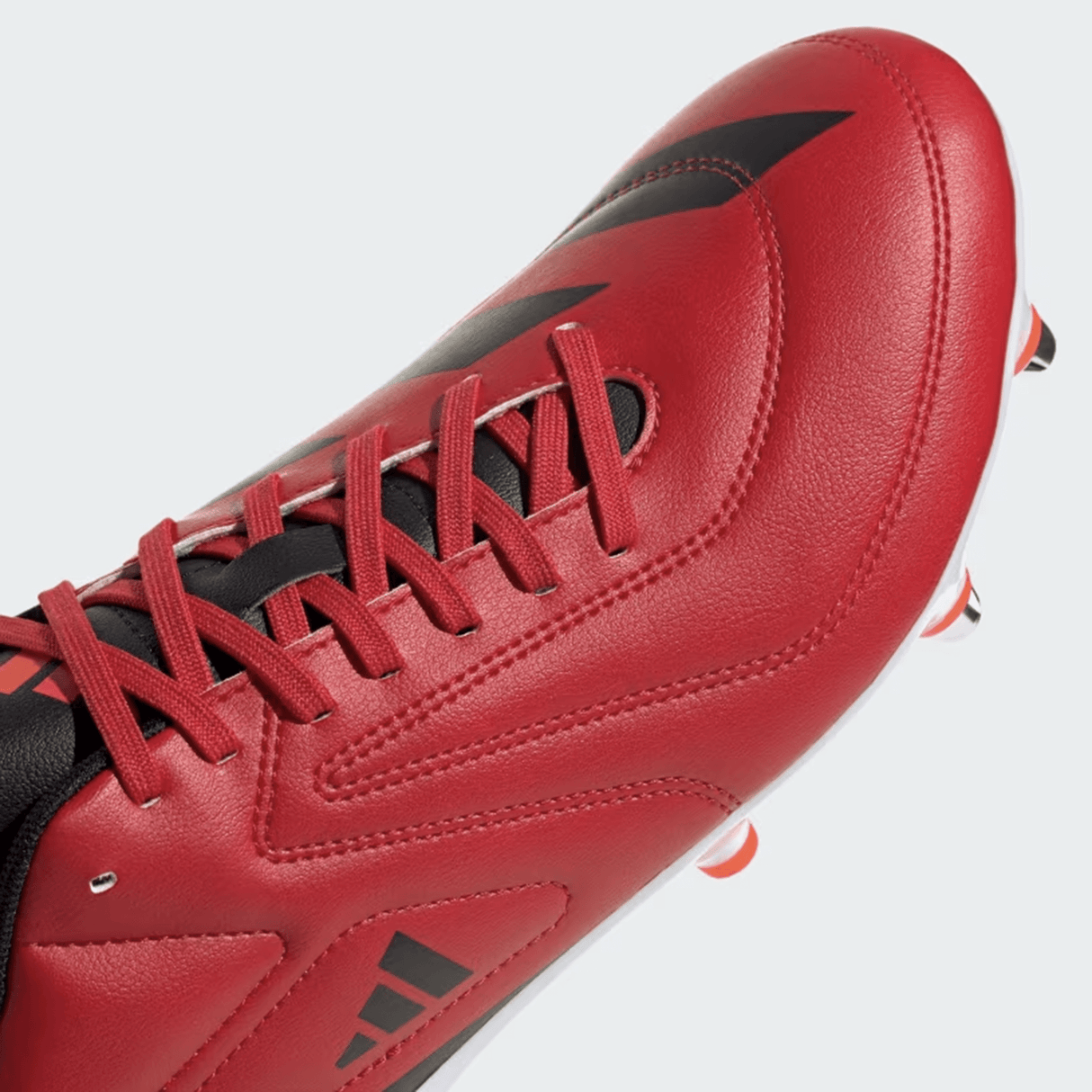 A close-up of the adidas RS15 SG 24 Rugby Cleat in Better Scarlet, Core Black, and Solar Red with laces, featuring a Speedframe outsole and small metal studs on the lightweight synthetic forefoot for grip.