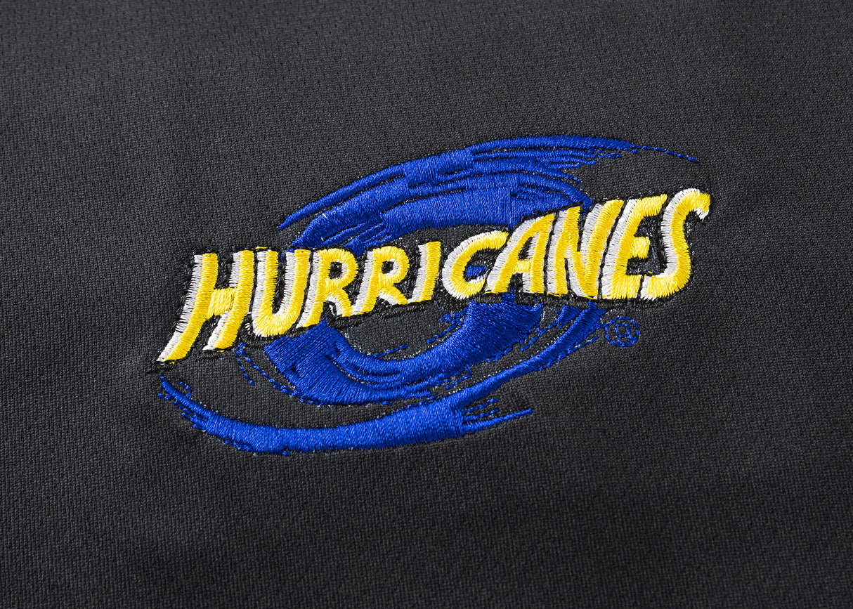 The Hurricanes Super Rugby 25/26 Team Polo by Classic Sportswear features a black fabric with a blue and yellow embroidered "Hurricanes" logo and stylized swirl, capturing the Hurricanes spirit for a classic sportswear look.