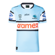 The Sharks NRL 25/26 Replica Home Jersey by Classic Sportswear features a light blue design with black and white striped sleeves, adorned with Pilot, Aramex, and Cronulla Sutherland Sharks logos. A must-have for any Sharks fan.