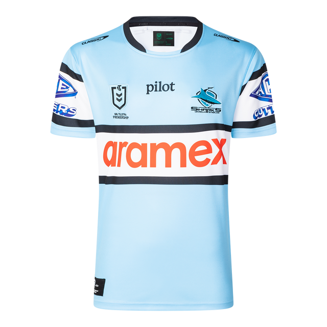 The Sharks NRL 25/26 Replica Home Jersey by Classic Sportswear features a light blue design with black and white striped sleeves, adorned with Pilot, Aramex, and Cronulla Sutherland Sharks logos. A must-have for any Sharks fan.