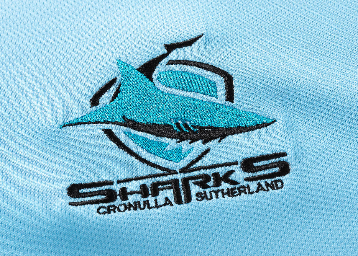 The Sharks NRL 25/26 Replica Home Jersey by Classic Sportswear features a light blue background, embellished with a blue shark logo and black "Sharks Cronulla Sutherland" text, embodying the team's spirit.