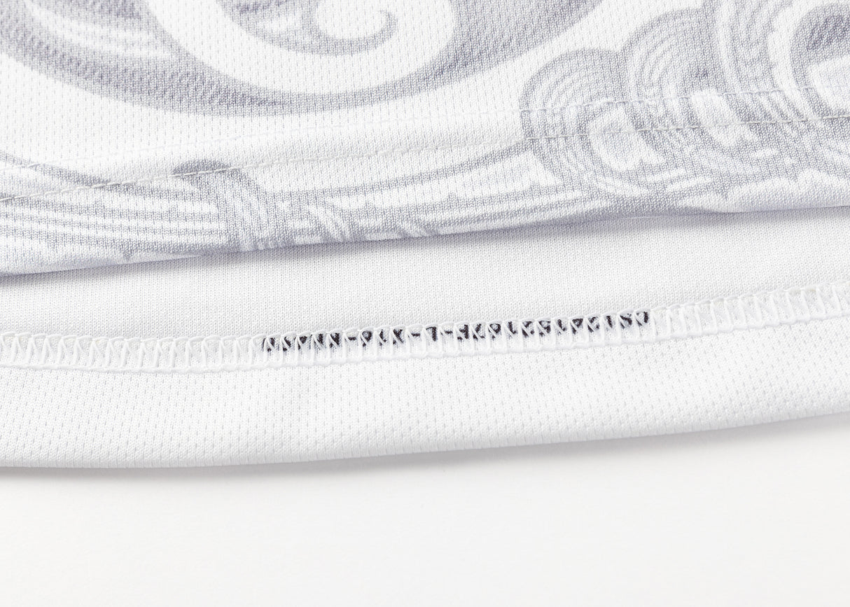 Close-up of a white fabric with decorative gray swirls and black text "www.pok-ta-pokwear.com.mx" along the seam, reminiscent of the intricate design on Classic Sportswear's Gallagher Chiefs Super Rugby Replica Away Jersey 25/26.