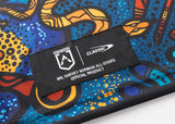 Close-up of a patterned fabric featuring a black label that reads "NRL Harvey Norman All-Stars Official Product" alongside the "Classic Sportswear" logo. The design boasts blue, orange, and red abstract shapes in the vibrant style of the NRL Indigenous All Stars 25/26 Replica Home Jersey by Classic Sportswear.