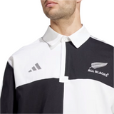 A person wears the All Blacks 24/25 Culture Jersey by adidas, a black and white rugby shirt with a collar, featuring the All Blacks logo and a small adidas logo adorned with the silver fern.