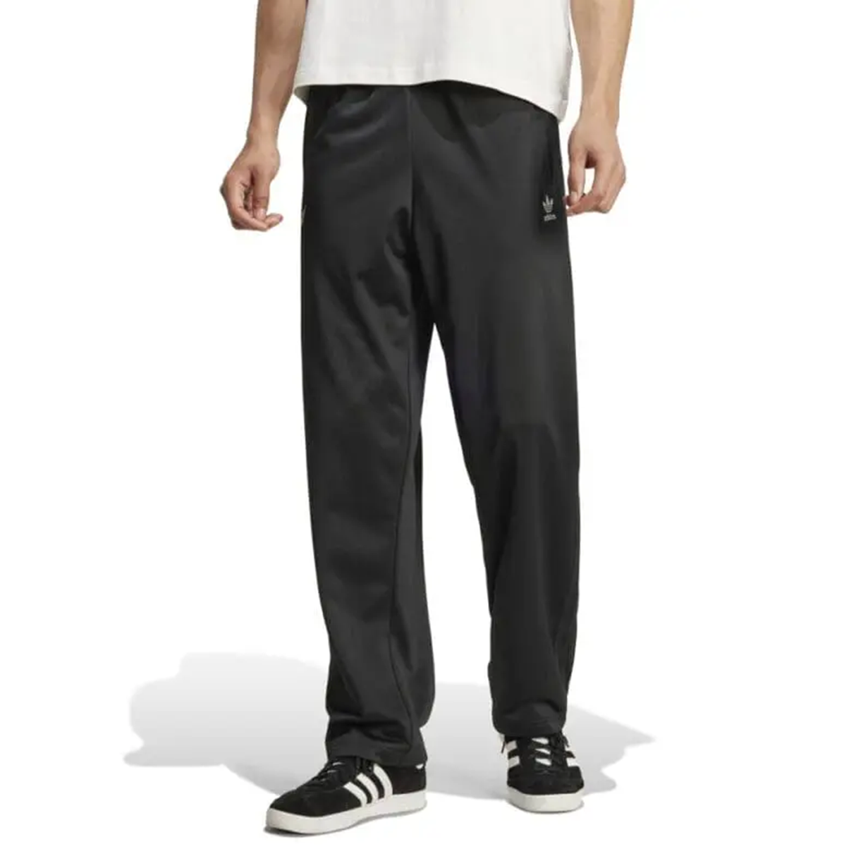 A person is wearing Originals Limited Edition All Blacks Firebird Track Pants by adidas, a crisp white shirt, and stylish black sneakers with white stripes.