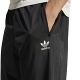 Someone wearing Adidas Originals Limited Edition All Blacks Firebird Track Pants, showcasing the brand's black design with a white logo, iconic three stripes, and zippered pocket.