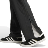 A person is wearing Originals Limited Edition All Blacks Firebird Track Pants by adidas, featuring classic white stripes and unzipped ankles, paired with black Adidas Gazelle sneakers with white accents, walking fluidly like an All Blacks player.