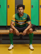 A man in an Admiral Nations of Rugby Jamaica Supporters Jersey sits on a bench in the locker room, surrounded by green and yellow lockers.