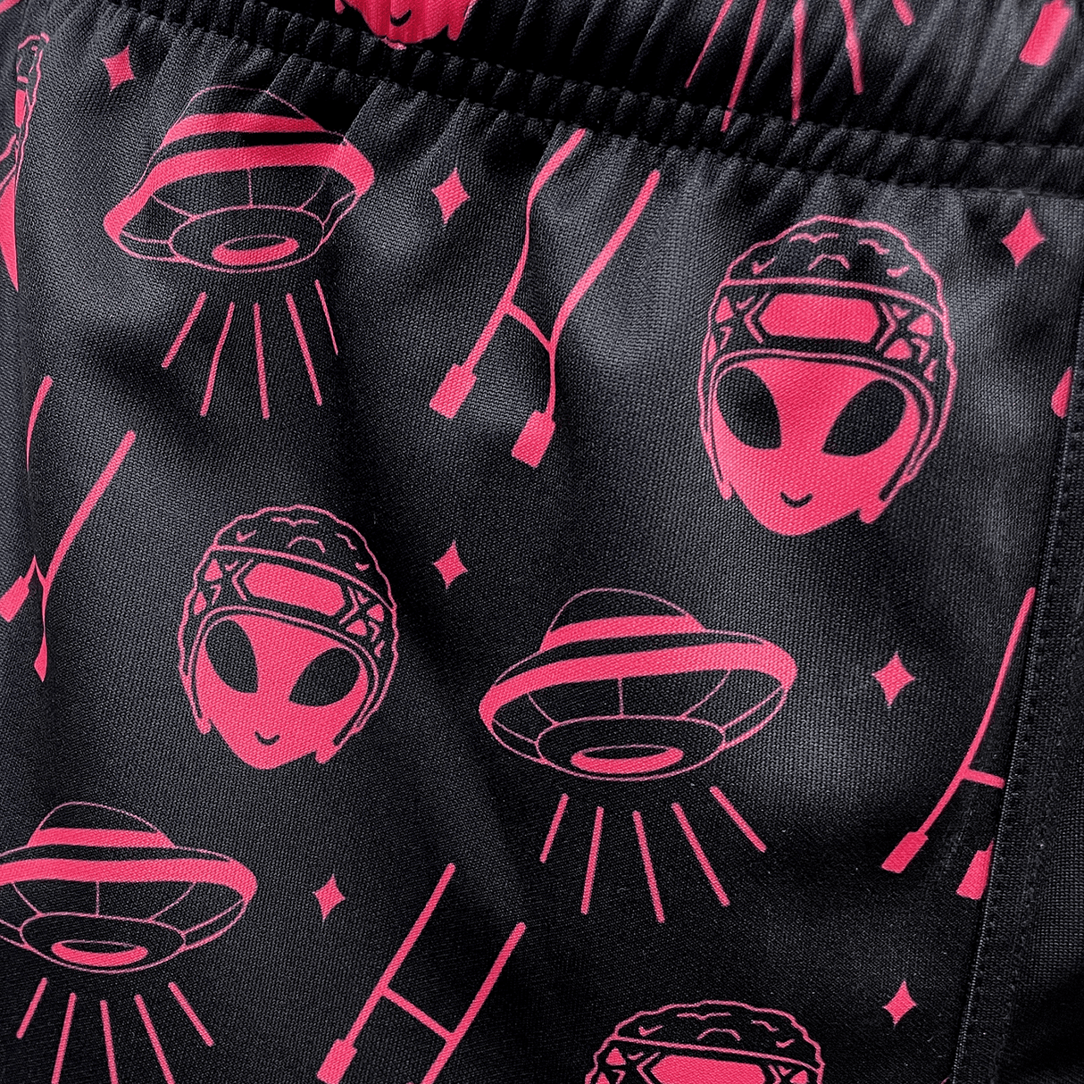 Close-up of the fabric for Modish Rugger's Limited Edition "We Scrum in Peace" Rugby Shorts, showcasing pink alien faces, UFOs, and stars on a black background.