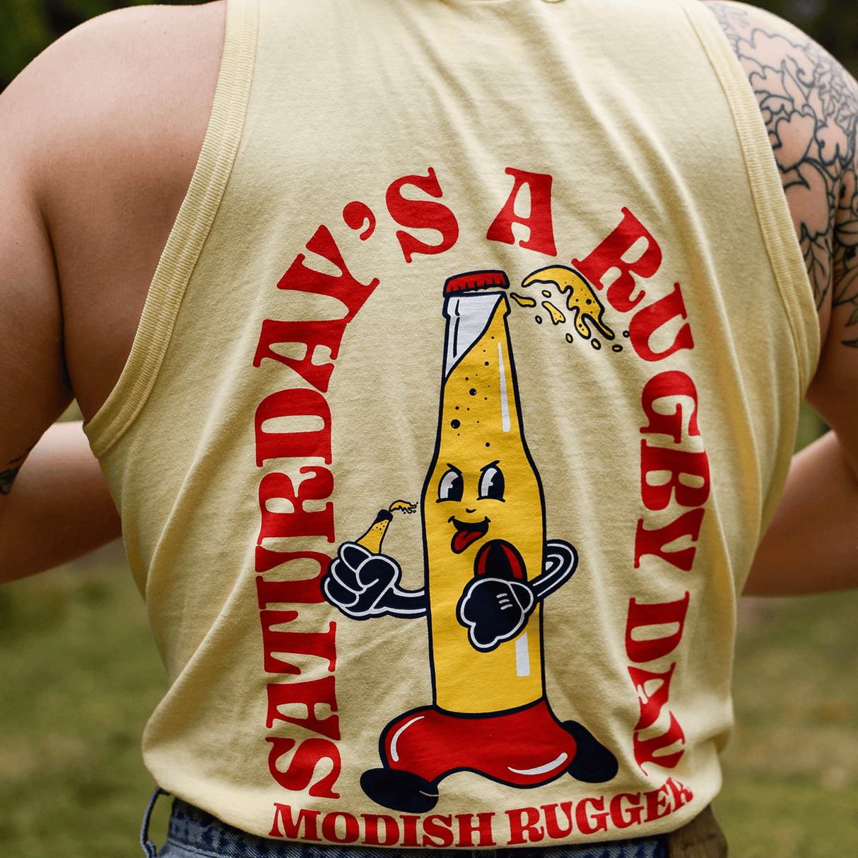 An individual is wearing the Modish Rugger Saturday's a Rugby Day Tank Top, which showcases a cartoon beer bottle graphic and text stating "Saturday's a Rugby Day.