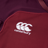 Close-up image of a maroon Canterbury Vapodri Evader Jersey with the Canterbury logo, featuring three white stylized "C" letters, stitched on the fabric. The jersey also boasts moisture-wicking technology and a Vapodri finish for optimal performance.