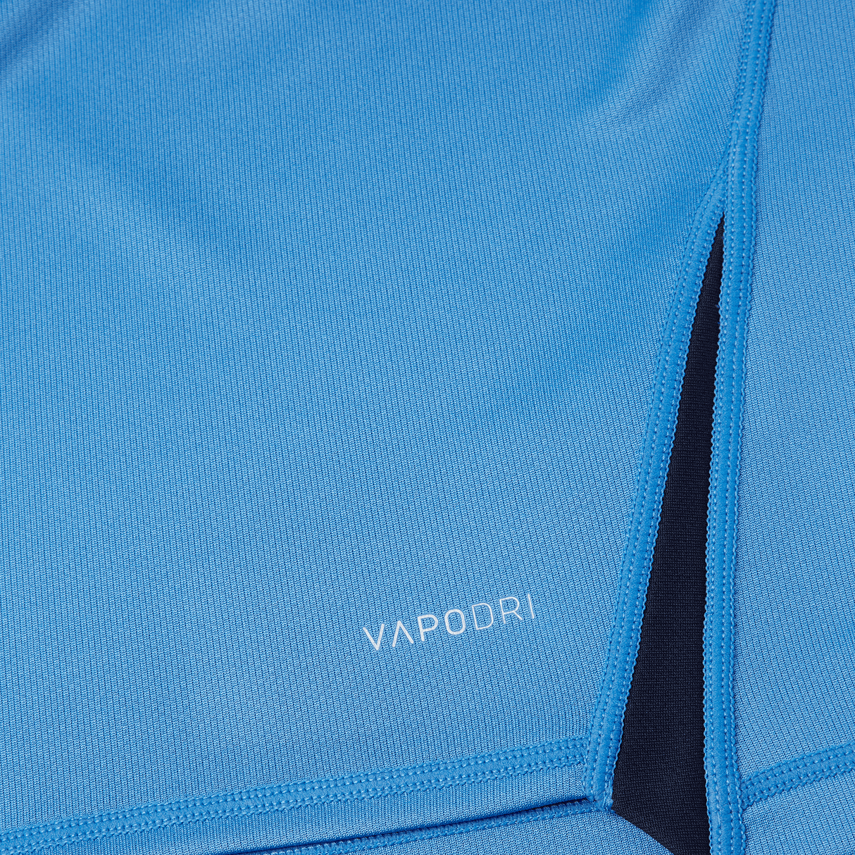 Close-up of a blue Canterbury Vapodri Evader Jersey made of breathable fabric with the word "VAPODRI" printed on it. A black inner lining is visible through a slit, showcasing the moisture-wicking technology of this Canterbury garment.