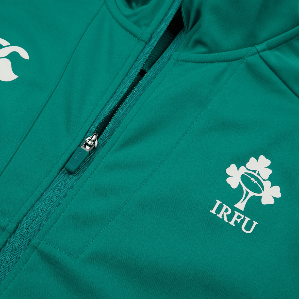 Here is a close-up of the green Ireland 24 Anthem Jacket by Canterbury with a zipper. It features a heat-pressed white IRFU clover and another white logo on one side. Crafted from water-resistant fabric technology, this jacket offers added durability.