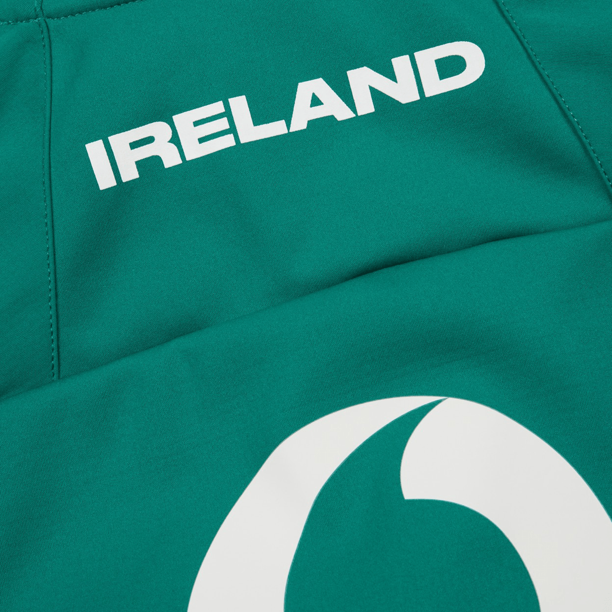 Close-up of the Ireland 24 Anthem Jacket by Canterbury, a green sports jersey featuring "IRELAND" printed in white capital letters at the top, with a partial white logo below. This jacket is crafted using heat pressed logos for durability.