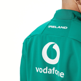 A person wearing the Ireland 24 Anthem Jacket by Canterbury in teal, featuring 'IRELAND' and 'vodafone' heat pressed logos on the back.