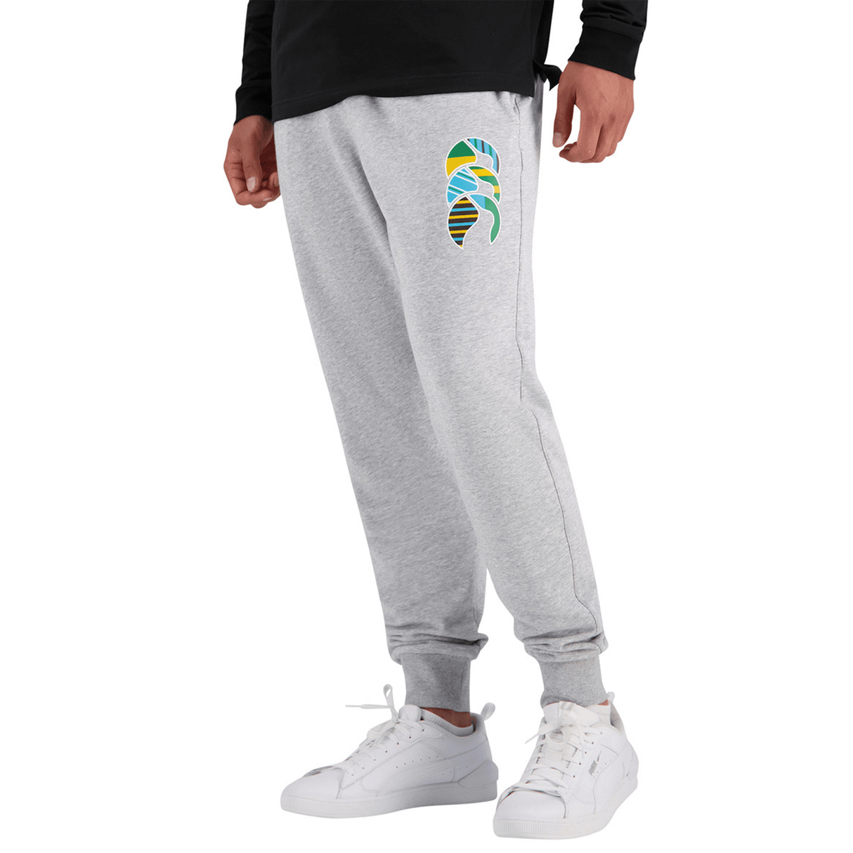 A person is wearing Canterbury Uglies Everyday Taper Leg Pants by Canterbury, which feature a colorful leaf design on the thigh, paired with a black shirt and white sneakers. These comfy sweatpants also include hip pockets and an elasticated waistband for added convenience.