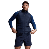 A man wearing a navy blue Canterbury Elite Microlite Gilet, navy blue long sleeve shirt, and black shorts standing with hands on hips.