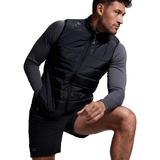 A man in athletic wear, featuring a black Canterbury Elite Microlite Gilet and gray long sleeve shirt, poses with one hand on his thigh.